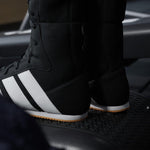 Black Adidas boxing boots with white stripes on a dark background